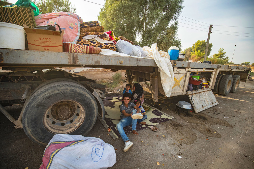 在敘利亞因流離失所者抵達塔爾塔梅爾時,一名婦女和兒童坐在一輛卡車下。